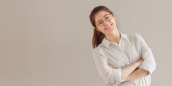 Junge Frau mit Brille steht lächelnd mit verschränkten Armen.